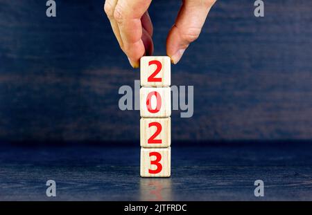 2023 felice anno nuovo simbolo. I cubi di legno simboleggiano il passaggio dal 2022 al nuovo anno 2023. Mano uomo d'affari. Splendido sfondo nero. Spazio di copia Foto Stock