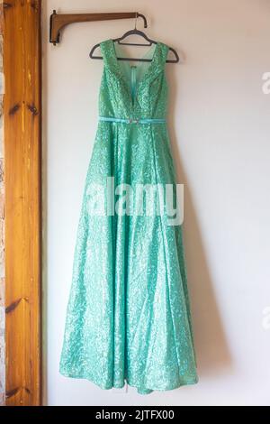 Un lungo vestito verde bridesmaid con ricami e paillettes è su un appendiabiti sulla parete Foto Stock