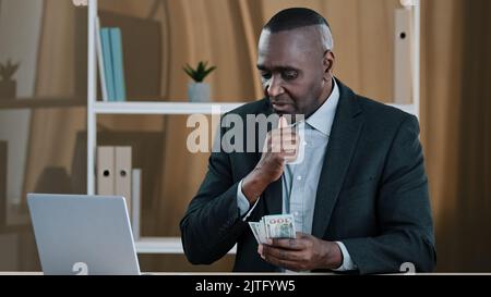 African vecchio maschio boss banchiere azienda CEO investitore senior maturo uomo d'affari conteggio di denaro in ufficio successo biracial uomo ricco in possesso di dollari Foto Stock