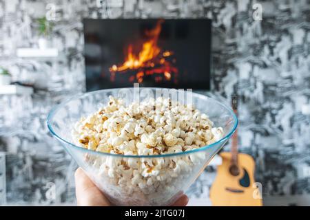 Una ciotola di vetro di popcorn e il telecomando in background il televisore funziona. Serata accogliente guardando un film o una serie TV a casa Foto Stock