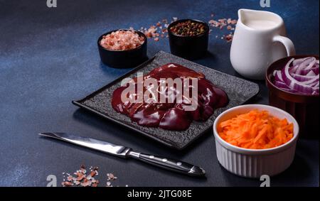 Pezzi di fegato crudo su un tagliere di legno contro uno sfondo di cemento scuro. Preparazione di pate epatico Foto Stock