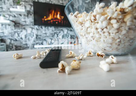 Una ciotola di vetro di popcorn e il telecomando in background il televisore funziona. Serata accogliente guardando un film o una serie TV a casa Foto Stock