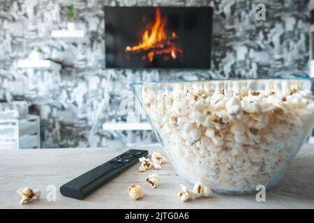 Una ciotola di vetro di popcorn e il telecomando in background il televisore funziona. Serata accogliente guardando un film o una serie TV a casa Foto Stock