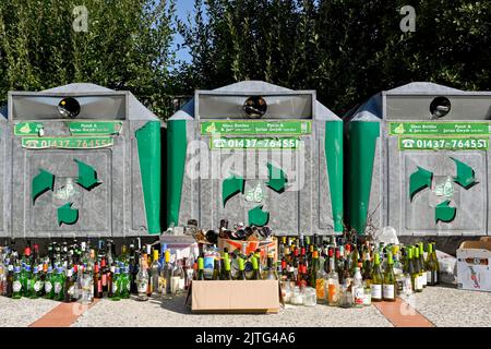 Newport, Pembrokeshire, Galles - Agosto 2022: Un gran numero di bottiglie di vino rimaste accanto ai contenitori di riciclaggio che sono pieni Foto Stock