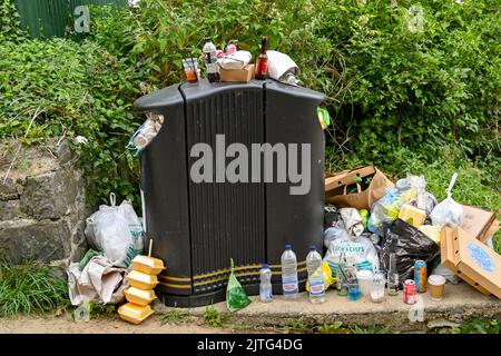 Newquay, Ceredigion, Galles - Agosto 2022: Sacchi, bottiglie e altri rifiuti impilati accanto a un cestino pieno Foto Stock