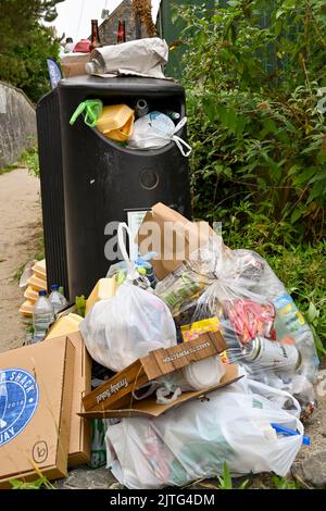 Newquay, Ceredigion, Galles - Agosto 2022: Sacchi, bottiglie e altri rifiuti impilati accanto a un cestino pieno Foto Stock