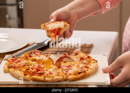 Fetta rialzata di pizza prima di mangiarla e stretching trefoli di formaggio Foto Stock