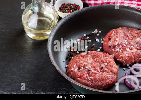 Hamburger di bistecca di manzo appena sminuzzato e crudo, con spezie in una padella, su un tavolo di ardesia nera, spazio copia, vista dall'alto Foto Stock