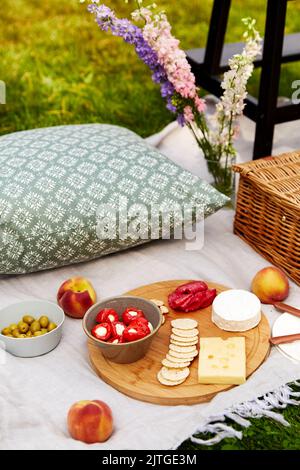 cibo, spuntini e cestino da picnic su coperta su erba Foto Stock