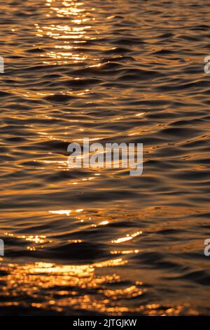 Ripple acqua mare oceano superficie con luce tramonto dorato. Primo piano dell'onda di mare Foto Stock