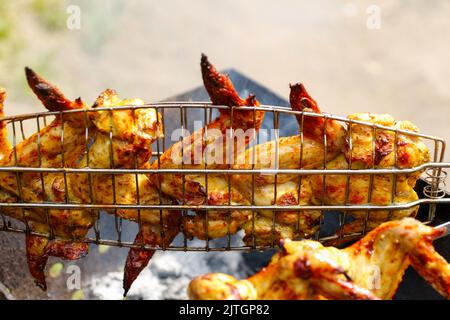 Sfocate il delizioso barbecue con ali di pollo sulla griglia calda. Le cosce e le ali di pollo vengono fritte su una braciere in una griglia per barbecue, marinata. Buffalo Foto Stock