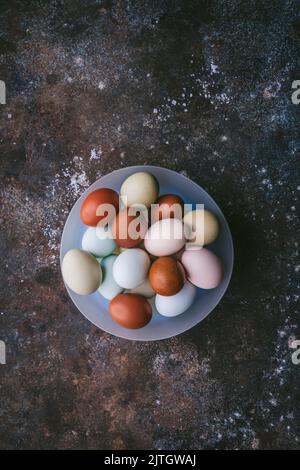 Piatto di uova di colore naturale in una ciotola di colore blu pallido su fondo scuro Foto Stock