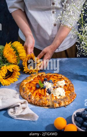 Donna che organizza girasoli e una galetta di albicocche intera con gelato e mirtilli freschi su un tavolo. Foto Stock