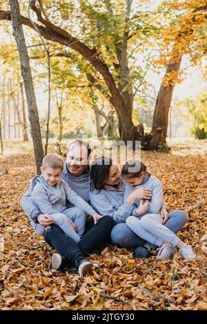 Ritratto di una famiglia con bambini in posa, giocando e divertendosi nel parco cittadino autunnale. Concetto di stile di vita della gente. Concetto di famiglia. Autunno Foto Stock