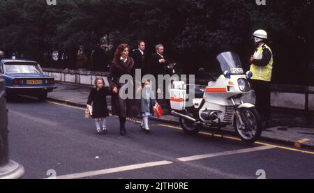 30 aprile 1980, Londra, Regno Unito: Donna che cammina con due bambini piccoli davanti a un ufficiale di polizia e una moto durante la protesta a Londra durante i sei giorni di assedio dell'Ambasciata iraniana. Dal 30 aprile al 5 maggio 1980, un gruppo di sei dissidenti iraniani armati, contrari all'Ayatollah Khomeini, leader religioso salito al potere nel 1979, ha rilevato l'ambasciata iraniana sulla porta del Principe a South Kensington, Londra. Il gruppo iraniano ha preso 21 ostaggi, due dei quali sono stati uccisi. Vicino alla scena dell'assedio, i sostenitori di Khomeini hanno reso note le loro opinioni con una protesta. Il drammatico assedio di sei giorni Foto Stock