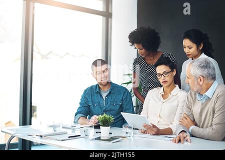 Considerando quale delle loro strategie potrebbe funzionare meglio, un gruppo di colleghi discuterà insieme di qualcosa su un tablet digitale. Foto Stock