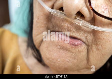 Faccia di primo piano della paziente anziana ammalata del sud-est asiatico con disturbi respiratori riposo a letto in ospedale Foto Stock