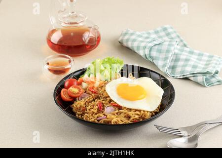 Indomie Goreng o mie Goreng, indonesiano popolare Instant Noodle. Servito con uovo di lato soleggiato, pomodoro, cetriolo. Copia spazio per testo Foto Stock