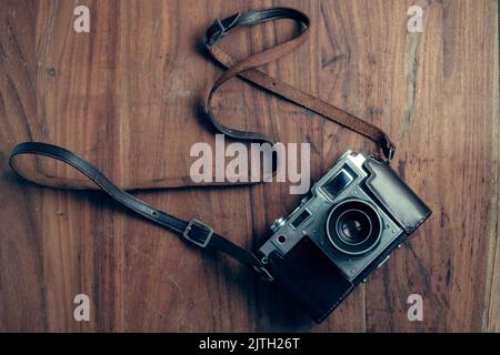 Una foto di una vecchia fotocamera con telemetro a pellicola vintage 35mm in una custodia in pelle originale, scattata su uno sfondo in legno testurizzato Foto Stock