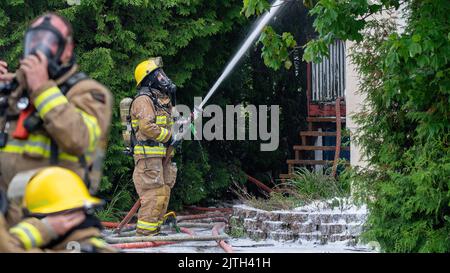 Rouyn-Noranda, Quebec, Canada - giugno 2022 : un pompiere che lotta contro un fuoco domestico durante il giorno, con l'apparecchiatura di protezione respiratoria Foto Stock