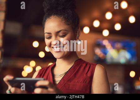Non può sopravvivere senza i social media al suo fianco. Una giovane donna che SMS su un cellulare in un bar. Foto Stock