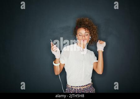 Suoni che si connettono con l'anima. Studio di una giovane donna attraente che ascolta musica sul suo telefono su uno sfondo grigio. Foto Stock
