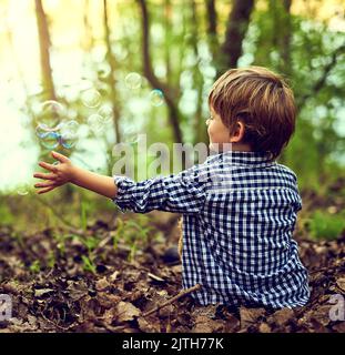 Galleggiando sul loro viaggio nel cielo, un ragazzino che gioca con le bollicine mentre si siede da solo nella foresta. Foto Stock