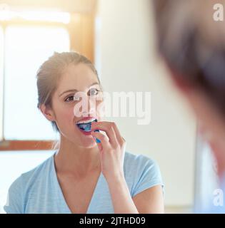 La spazzolatura è importante per gengive e denti sani. Una giovane donna che le sfrega i denti in uno specchio. Foto Stock