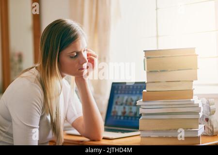Essere uno studente succhia a volte. Una giovane donna che guarda sopraffatto dal mucchio di libri sulla sua scrivania. Foto Stock