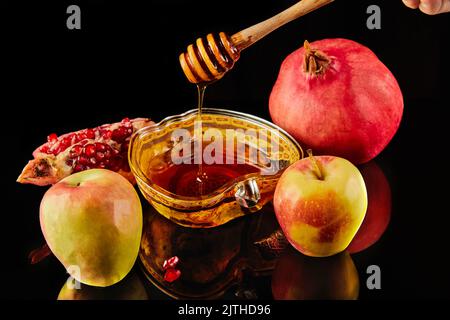 Rosh hashanah - concetto ebraico di vacanza di nuovo anno. Ciotola a forma di mela con miele, mele, melograni, shofar su sfondo nero con riflesso Foto Stock