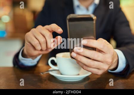 Invio di un aggiornamento di testo. Un uomo d'affari irriconoscibile che invia un messaggio di testo mentre è seduto in un bar. Foto Stock