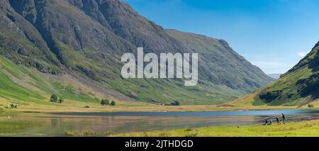 Clencoe,Lochaber,Scozia,Regno Unito-Agosto 22 2022: Lungo la valle di Glen Coe, la giovane famiglia gode di vedute sul Loch, miniaturizzato dal drammatico Foto Stock