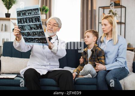Maturo anziano attraente alto-esperto medico premuroso maschio che spiega i risultati dell'immagine di MRI di raggi X al suo paziente malato del bambino e a sua madre durante la visita loro nel paese. Tomografia computerizzata. Foto Stock