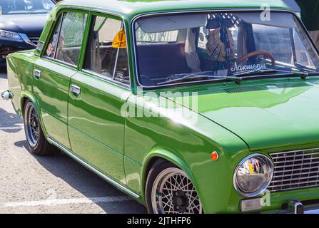 Restyling di vecchia automobile sovietica. Vista frontale di un'auto d'epoca parzialmente verde su una strada soleggiata all'aperto. Sul parabrezza di auto divertente iscrizione in russo lusso. TR Foto Stock