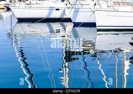 Gli yacht a vela ormeggiati nel porto turistico in una giornata di sole si riflettono nell'acqua di mare increspata. Foto di sfondo astratta Foto Stock