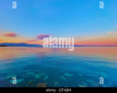 Il pittoresco tramonto sul Lago di Garda con la sua superficie ondulata e le sagome delle Prealpi del Garda sullo sfondo, Desenzano del Garda Foto Stock