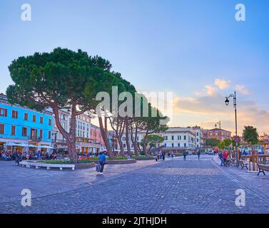 DESENZANO DEL GARDA, ITALIA - 10 APRILE 2022: Il lungolago con le antiche case, i ristoranti, i pini sparsi e le aiuole Foto Stock