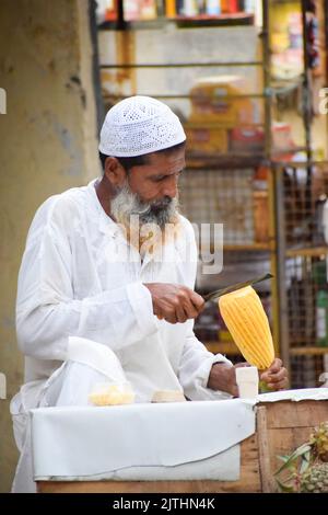 Un uomo musulmano che si stacca la pelle di ananas per vendere in strada Foto Stock