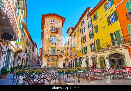La piccola area con tavoli di ristoranti all'aperto, decorata con fiori in vaso, circondata da case storiche di Via Vicolo due Torri, Bresci Foto Stock