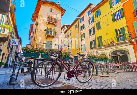 La bici parcheggiata presso il ristorante all'aperto con posti in pentole e case storiche colorate sullo sfondo, Brescia, Italia Foto Stock