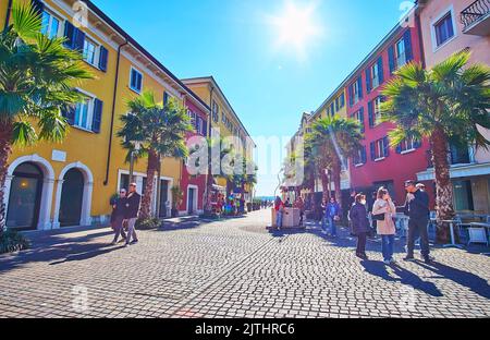 SIRMIONE, ITALIA - 10 APRILE 2022: Il cielo soleggiato sopra la panoramica piazza pedonale Piazza Castello con le linee di palme verdi e case colorate, il mese di aprile Foto Stock