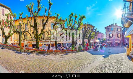 Panorama della vecchia stretta Via San Salvatore con alberi sparsi, terrazze all'aperto di caffè e ristoranti di fronte alle case storiche di Sirmio Foto Stock