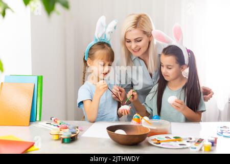 Giovane madre e le sue due figlie di pittura delle uova di Pasqua Foto Stock