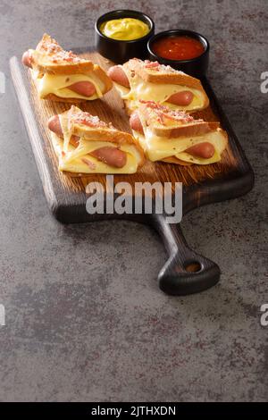 Toast caldo con salsicce e formaggio servito con ketchup e senape primo piano su un asse di legno sul tavolo. Verticale Foto Stock