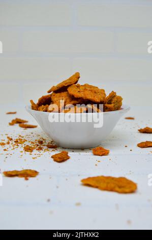 Patatine di tempeh gustose e deliziose in una ciotola con fondo bianco. Vuoi uno spuntino saporito e croccante? I chip tempeh sono la risposta. Foto Stock