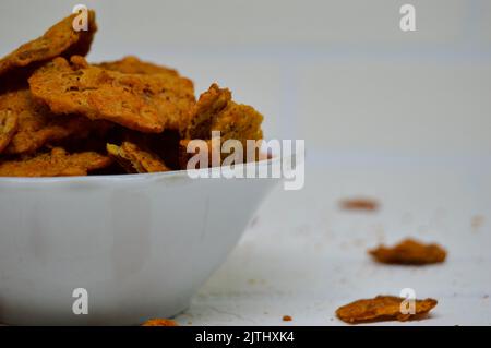 Patatine di tempeh gustose e deliziose in una ciotola con fondo bianco. Vuoi uno spuntino saporito e croccante? I chip tempeh sono la risposta. Foto Stock