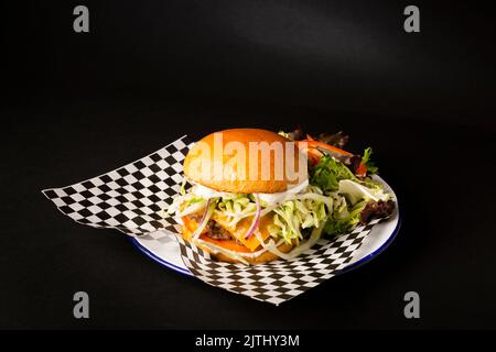 Due hamburger schiacciati con formaggio accompagnato da patatine fritte su un piatto bianco su sfondo nero Foto Stock