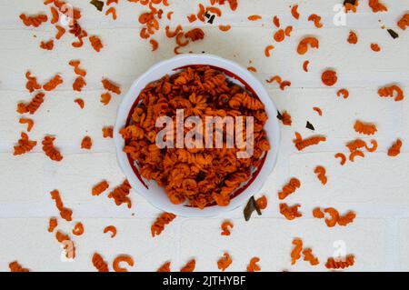 Maccheroni piccanti e saporiti in una ciotola su fondo bianco. I maccheroni secchi hanno una sensazione diversa quando vengono consumati come snack. Foto Stock