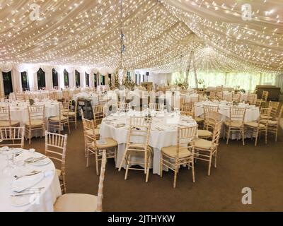 Il Marquee è decorato per un matrimonio con luci da fava, tovaglie bianche e sedie. Foto Stock