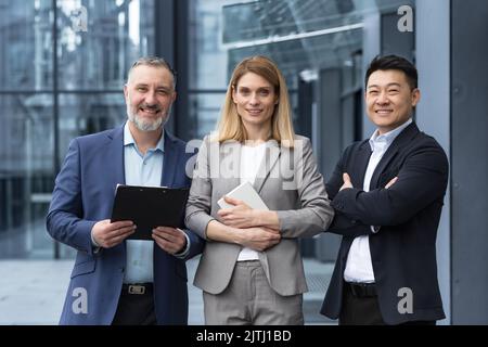 Team di sogno di successo, gruppo di business diversificato di uomo asiatico e donna d'affari sorridente e guardando la macchina fotografica, colleghi con braccia incrociate al di fuori degli uffici, professionisti investitori e banchieri Foto Stock